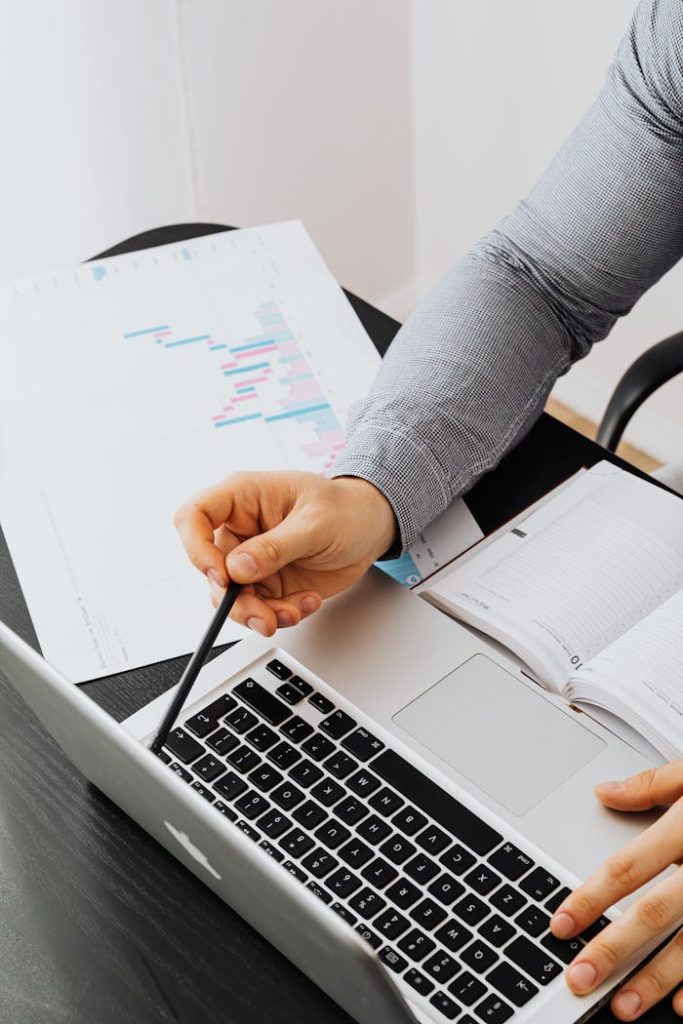a-person-holding-a-pen-5717715 Business professional analyzing charts and data on a laptop in office setting.