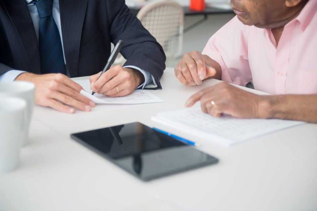hands-of-men-in-office-8441782 Two professionals discussing and signing documents in a business meeting.